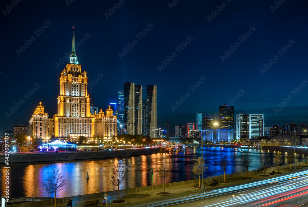 Night view of high-rise stalinist building and Moscow river with Moscow City buildings in the background in Moscow, Russia.