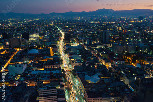 Aerial View of Mexico City at Dusk with Illuminated Streets and Distant Mountains.
