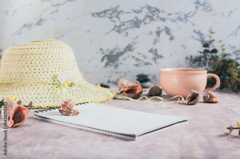 Travel planning notebook, hat, seashells and cup of coffee on table