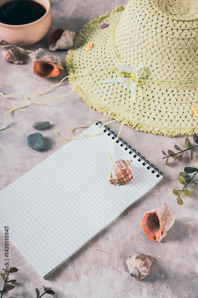 Notebook, beach hat, shells and stones on the table vertical view