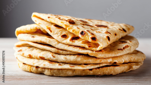 Healthy recipes,  high fiber and grains. A stack of freshly cooked flatbreads, folded and placed on a wooden surface, displaying a golden-brown, slightly charred texture.