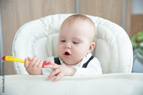 Cute baby with spoon sitting at feeding table