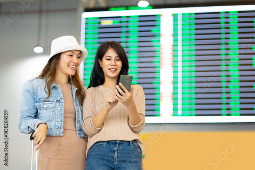 Obraz na płótnie Check flight schedule on board with information display. arrival and departure board. Two Asian woman use smartphone cheking flight for travel in long weekend w salonie