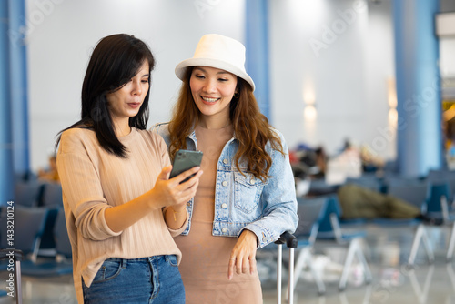 Obraz na płótnie Internet Online Check flight schedule on smartphone. arrival and departure board. Two Asian woman use smartphone cheking flight for travel in long weekend w salonie