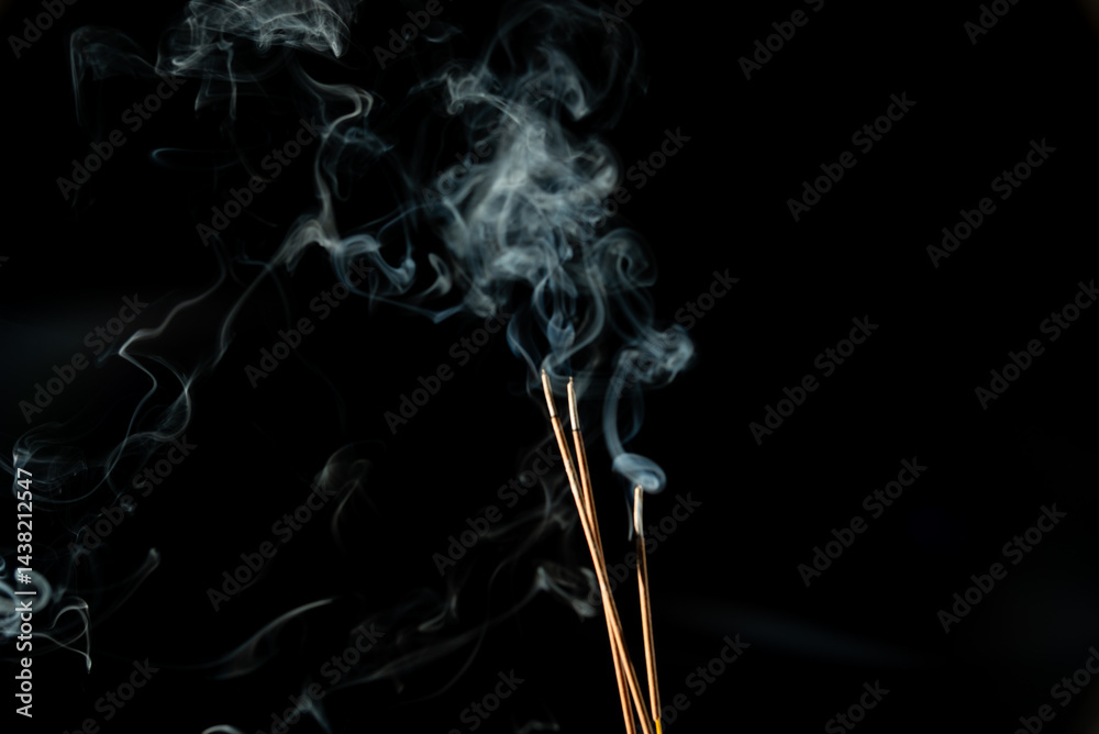 Three burning incense sticks with smoke on a black background. Three burning incense sticks with smoke on a black background.