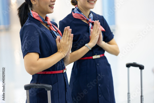 Obraz na płótnie Portrait two woman friends sawasdee thai hello in airport. Cabin crew, air hostess working in airplane. Service mind. Asian stewardess with suitcase at modern airport terminal. flight attendant w salonie