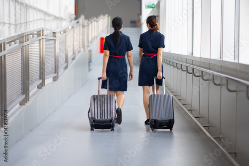 Obraz na płótnie Rear view Two woman friends walking in airport. Cabin crew, air hostess working in airplane. Service mind. Asian stewardess with suitcase at modern airport terminal. flight attendant w salonie