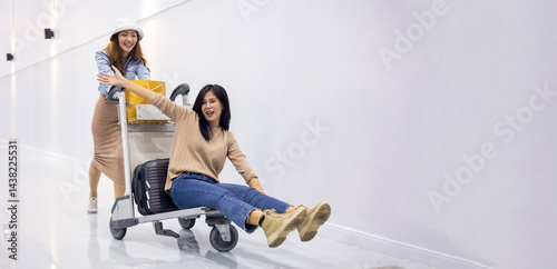 Riding baggage trolley. two Happy Asian beautiful woman passenger traveler and friends having fun with luggage at the airport