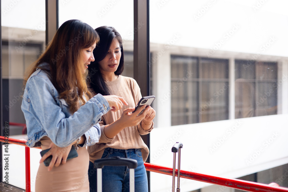 Two Asian Woman waiting for flight at airport lounge. Happy asian woman passenger traveler waiting for departure with suitcase at modern airport terminal