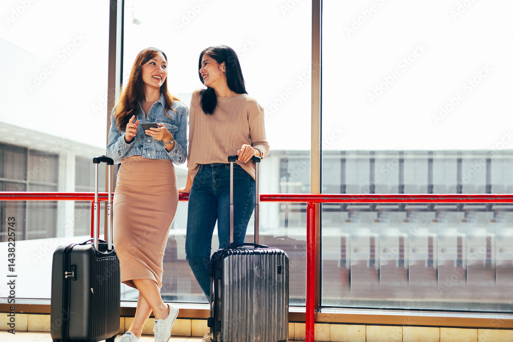 Two Asian Woman waiting for flight at airport lounge. Happy asian woman passenger traveler waiting for departure with suitcase at modern airport terminal