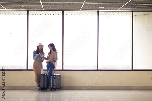 Two Asian Woman waiting for flight at airport lounge. Happy asian woman passenger traveler waiting for departure with suitcase at modern airport terminal