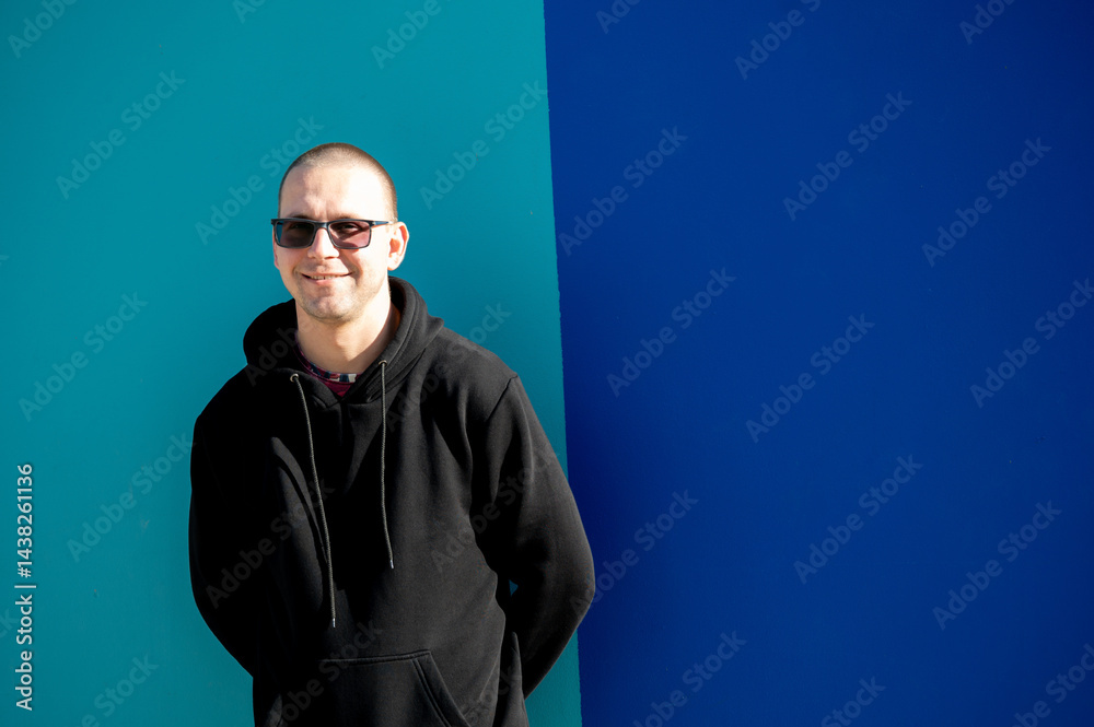 Stylish guy in glasses and black sweatshirt isolated on plain bright blue background, pointing with hand to side empty space for table or graph. Photo of model on wall background with empty space