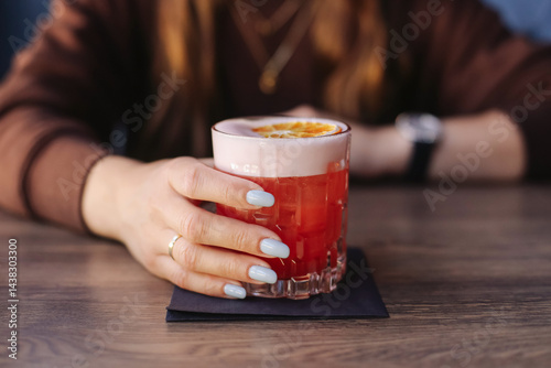 Obraz na płótnie Refreshing red cocktail with foam. Elegant drink with citrus slice. Woman hand holding glass. Summer party drink. Fresh fruity cocktail. Modern bar atmosphere. Colorful evening beverage background. w salonie
