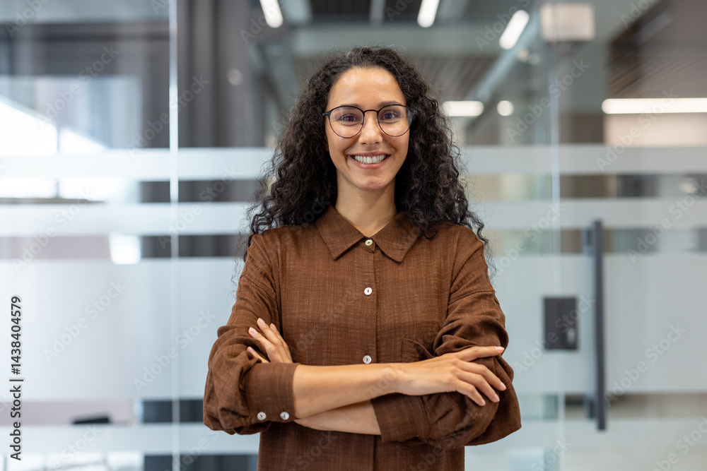 Portrait of successful joyful businesswoman at workplace inside office. Woman satisfied with achievement results looking at camera with crossed arms.