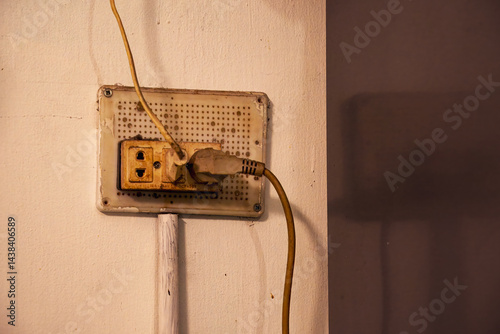 Old Electric Outlet with Plugged Cords on a Wall Indoors