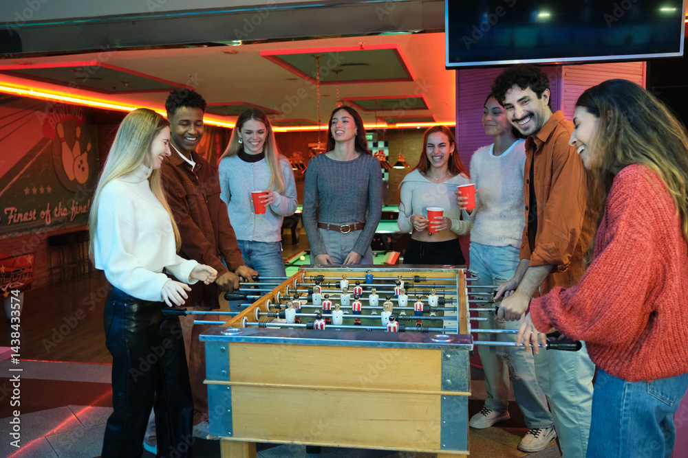 Group of friends having fun playing table football and drinking beer in a bowling club