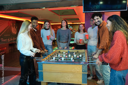 Obraz na płótnie Group of friends having fun playing table football and drinking beer in a bowling club w salonie