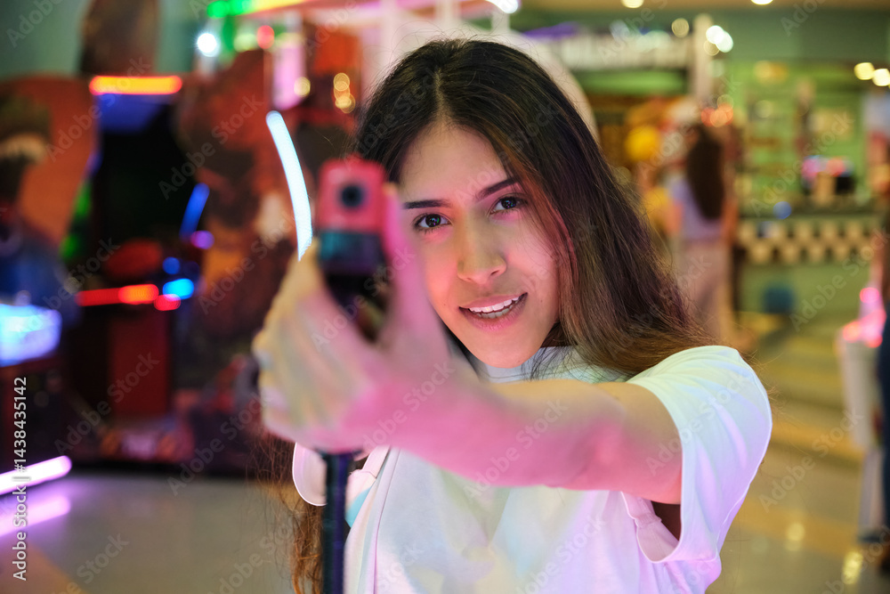 Young woman having fun playing arcade shooting game with toy gun in entertainment center