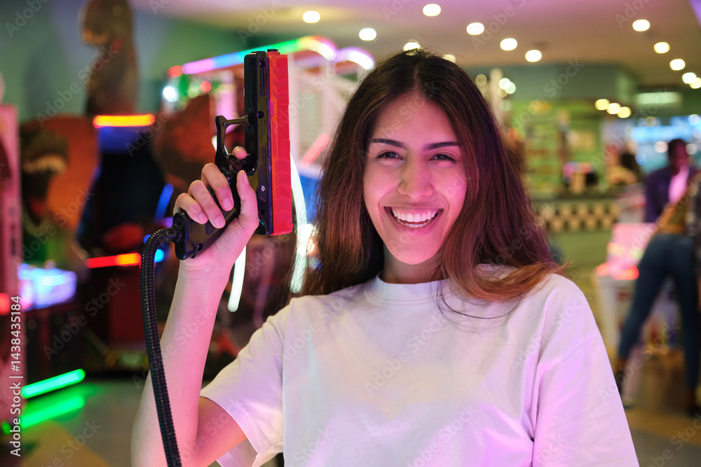 Young woman having fun playing in an arcade center holding a toy gun and smiling