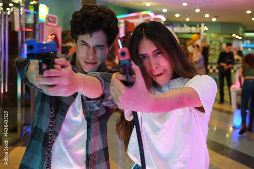 Young man and woman having fun playing with toy guns in an arcade