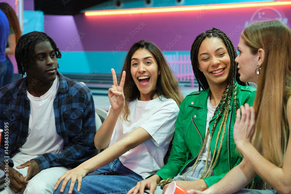 Young people enjoying time together at bowling club, gesturing victory sign and laughing