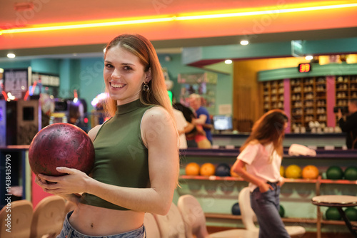 Obraz na płótnie Happy young woman holding bowling ball, smiling in bowling alley, ready for a game with friends w salonie