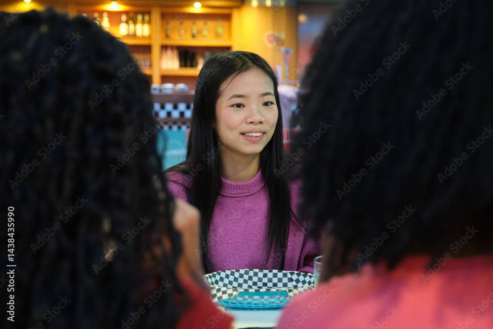 Asian woman enjoying a meal with friends at a diner, engaging in conversation and creating a warm, social atmosphere