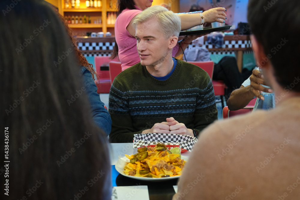 Group of friends enjoying a plate of nachos in a restaurant with fifties style decor