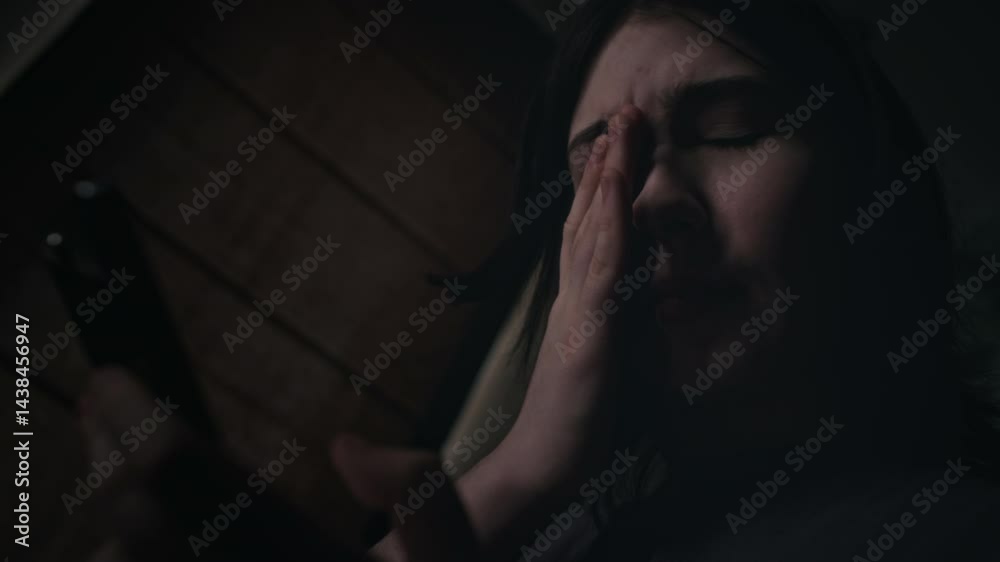 Low Dutch angle close-up of sobbing teenage Caucasian girl typing messages on smartphone, wiping off tears, due to harassment, bullying, blackmail, or talking to boyfriend over relationship breakup