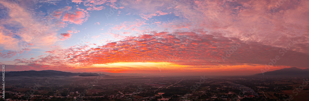 Fototapeta premium A breathtaking sunrise illuminates a small village nestled among lush green fields and karst mountains, with vibrant clouds filling the sky. The harmony of rural life set dramatic natural formations.