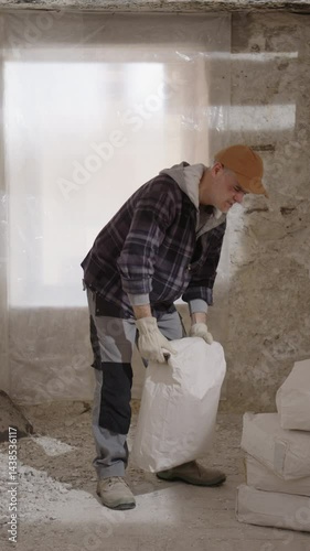 Construction builder worker on a building site lifting a heavy bag, suddenly experiencing back pain and a strained back injury due to poor posture, the importance of proper posture during heavy work