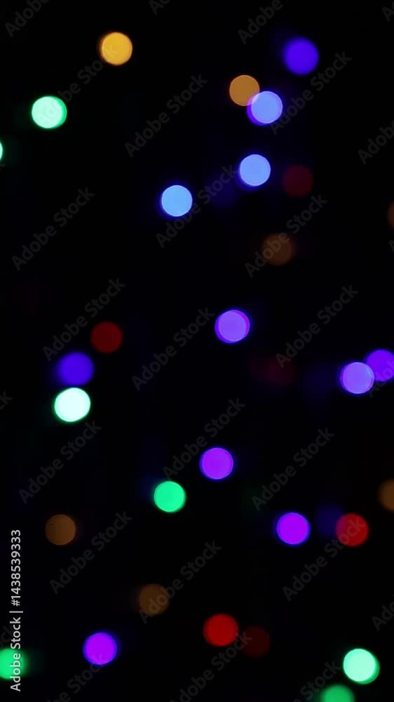 Una toma de cerca de varias luces de colores en forma de círculos en movimiento en la oscuridad. Desenfoque, efecto Bokeh. Video vertical
