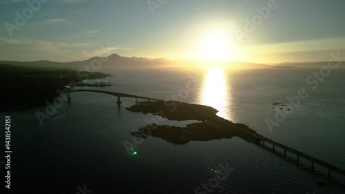 sunset over the sea with a bridge and mountains in the background