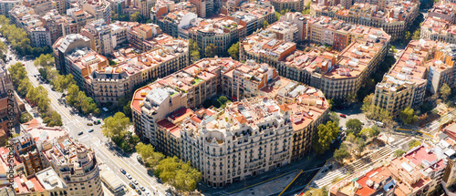 Aerial view of Barcelona's Eixample district with grid streets, green avenues, and historic buildings on a sunny day.