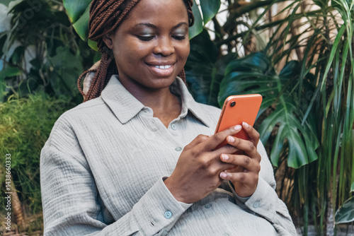 An African-American woman with a smartphone sits among beautiful lush greenery