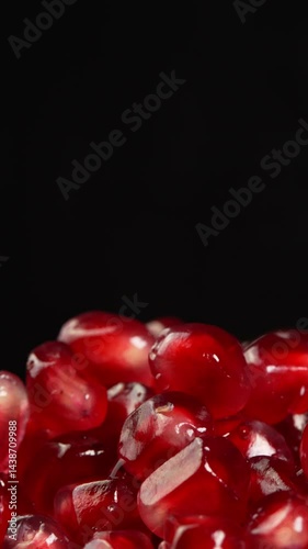 Vertical video Pomegranate seeds rotate on black background close up showcasin. Ruby pomegranate grains or garnet in low light for advertising and promotions. Juicy grenadine fruit natural antioxidant