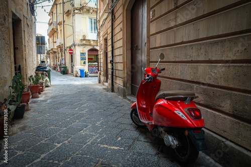 Fototapeta Naklejka Na Ścianę i Meble -  Narrow street in the old town of Syracuse in Sicily, Italy in a beautiful summer day. Travel and sightseeing journey concept. Motorbike parked beside the wall.