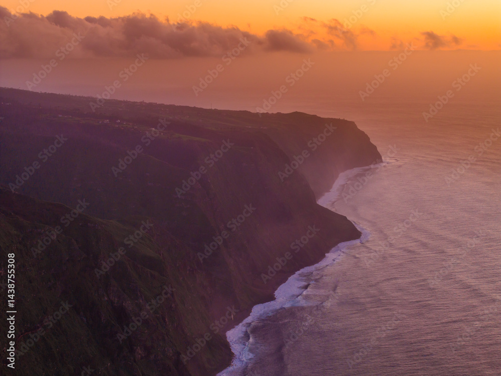 Dramatic cliffs meet the ocean at sunset, casting a warm glow over the rugged coastline of a remote paradise