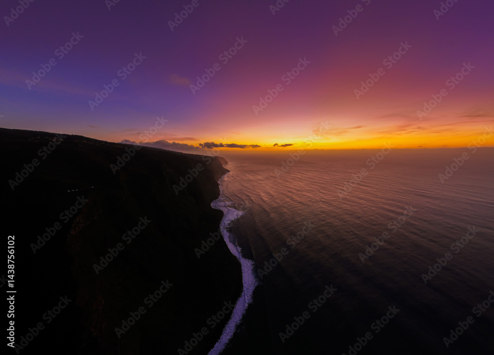 Golden hues paint the horizon as the sun sets over a tranquil ocean and rugged coastline