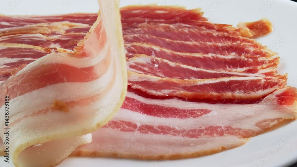 Grill tongs place a strip of raw bacon from the packaging. Pork meat with fat marbled within succulent meat. Slices of fresh smoked bacon for making English breakfast