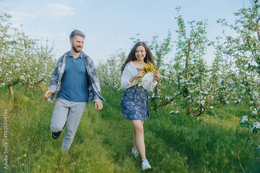 Obraz premium Happy Couple Running Through Blooming Orchard on a Sunny Spring Day