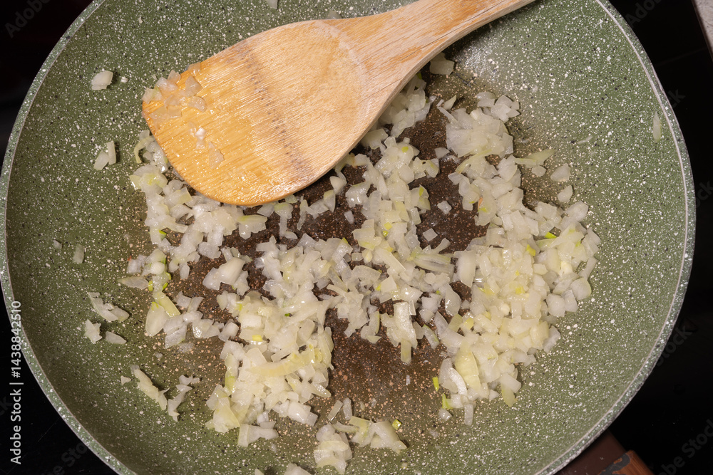 Diced onions sauteing in a pan, lightly cooked and turning translucent. A wooden spatula rests in the pan. A wooden spatula rests in the pan, showcasing the initial step in building flavors for recipe