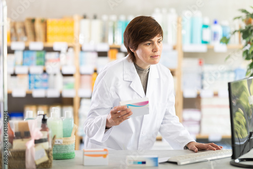 Professional female pharmacist working at counter in drugstore, verifying medicines information on computer and offering to customer, providing reliable healthcare advice