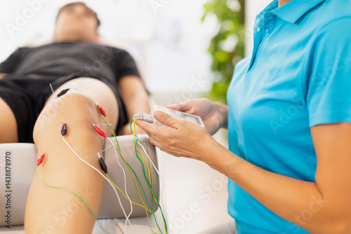 A physiotherapist applies electrostimulation to a patient's muscle and leg, using needle electrodes, with TENS, galvanic or trabert current
