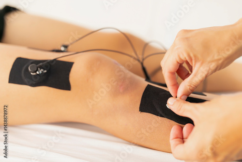 Fotografia A physiotherapist places the electrodes on the leg of a young patient during an