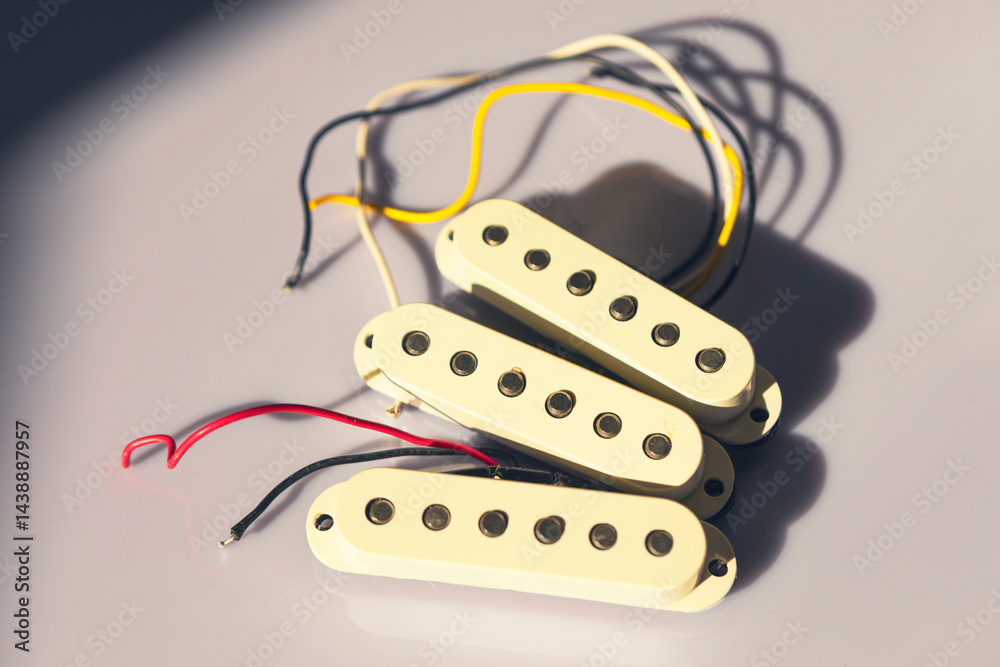Single-coil guitar pickups with cream-colored covers and visible pole pieces are placed on light surface, casting shadows. Wires extend from each pickup, indicating they are ready for installation
