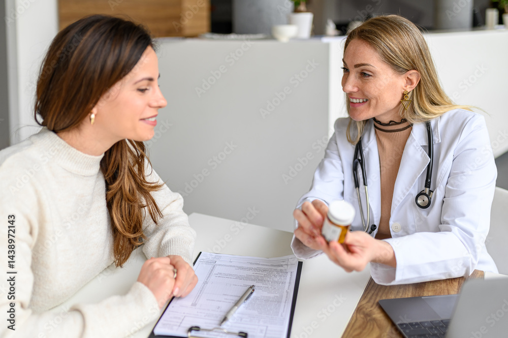 Fototapeta premium Smiling female doctor giving medicine bottle and explaining dosage to patient at desk in medical clinic