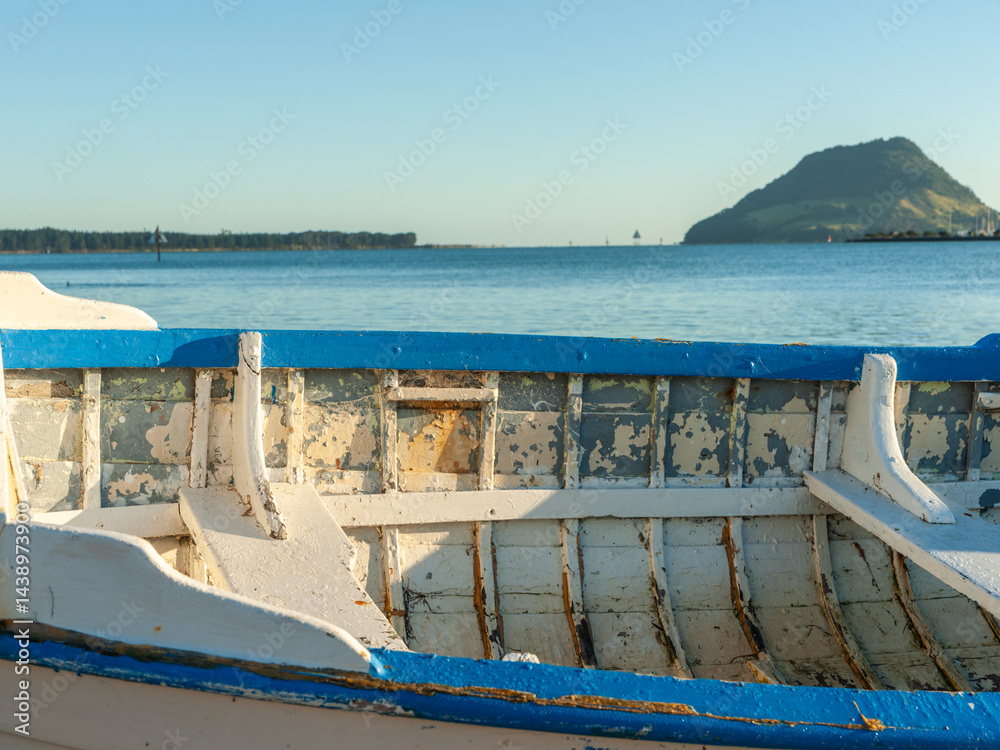 Old blue and white wooden clinker dinghy on beach at mid-tide with landmark Mount Maunganui in background