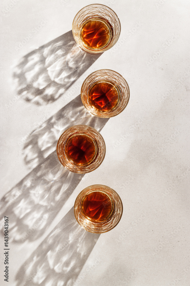 Transparent alcohol Glasses with dark shadows at sunlight on beige table, top view minimal lifestyle, aesthetic flat lay shiny glass sparkling at sun, summer strong drink, copyspace, vertical