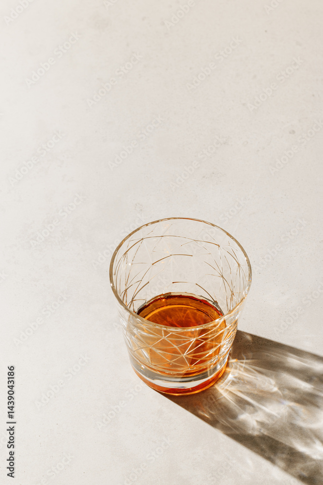 Crystal Glass with drink, beautiful shadow at sunlight on beige textured background, minimal trend, aesthetic side view shiny glass, sun glare, strong alcohol drink concept, summertime, copyspace